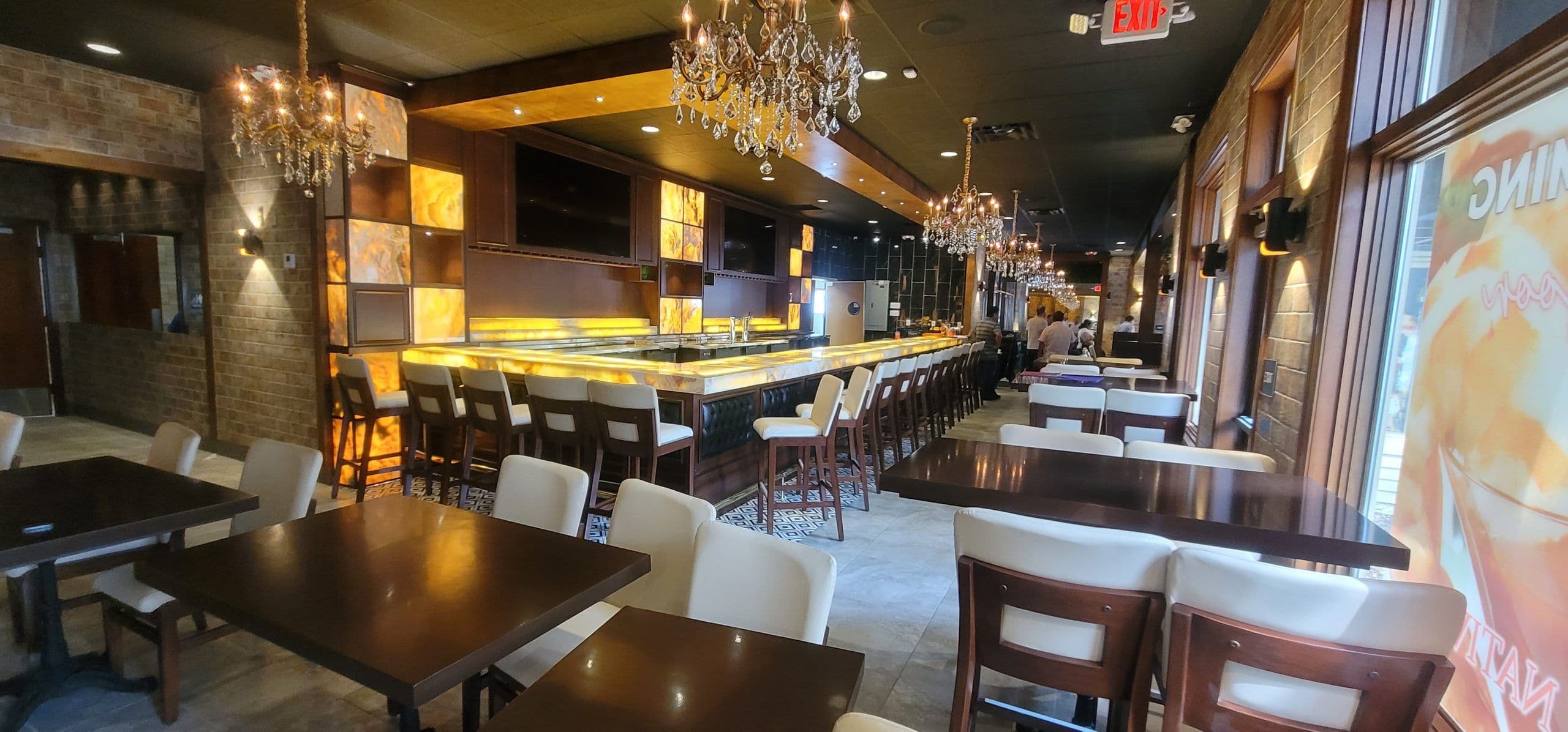 Finished bar and dining room at Nativos 614 in Columbus, a long backlit onyx bar with white leather stools, crystal chandeliers and exposed brick walls.